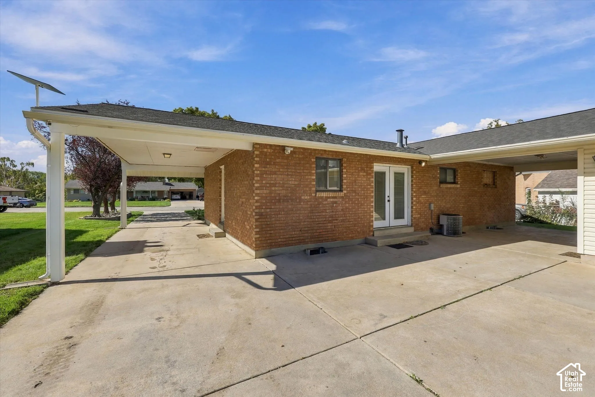 Brick exterior facade featuring a dual carport, expansive concrete driveway, and white-framed French doors