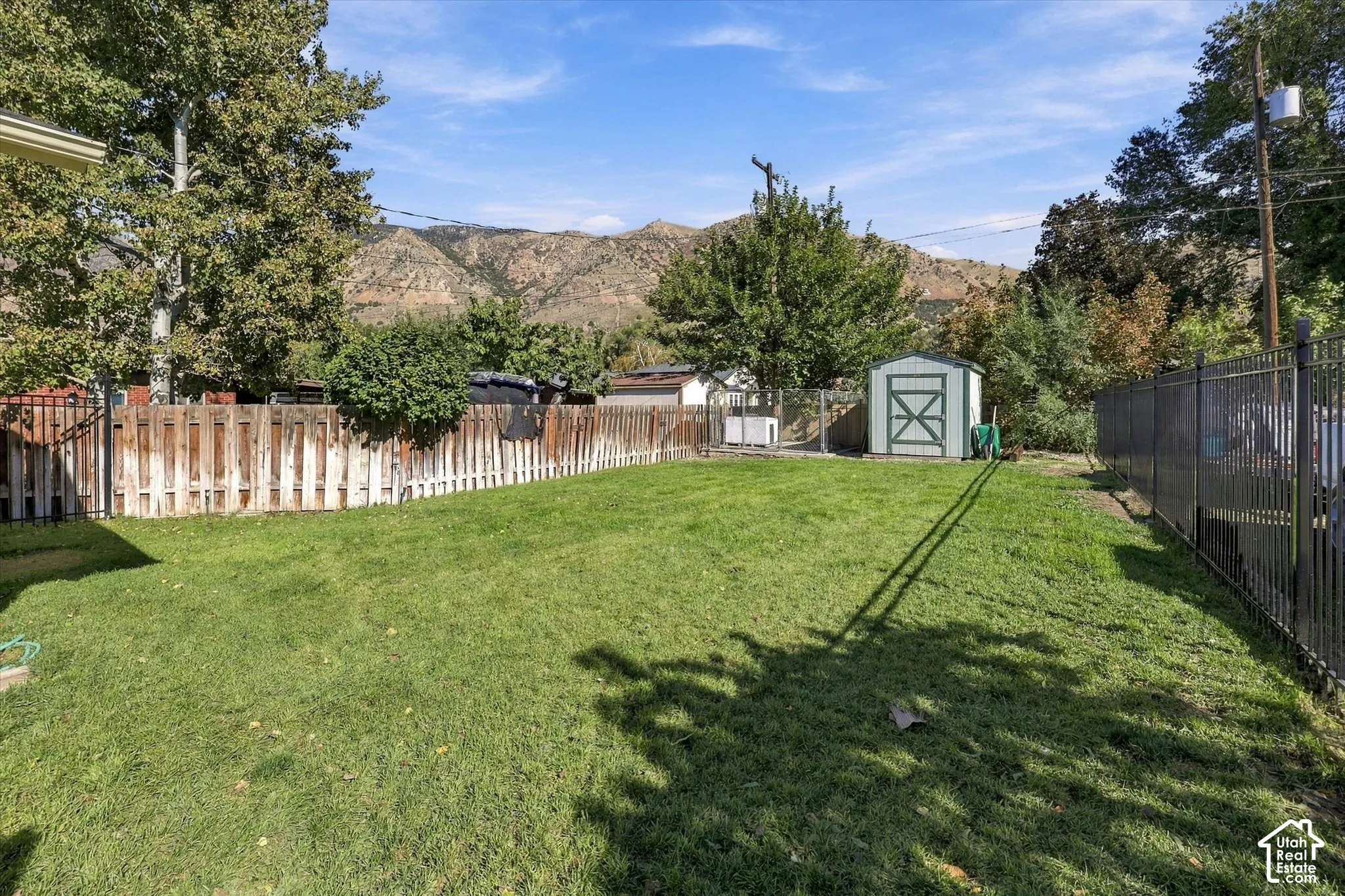 Fenced backyard featuring a manicured lawn, detached storage shed, and mountain backdrop