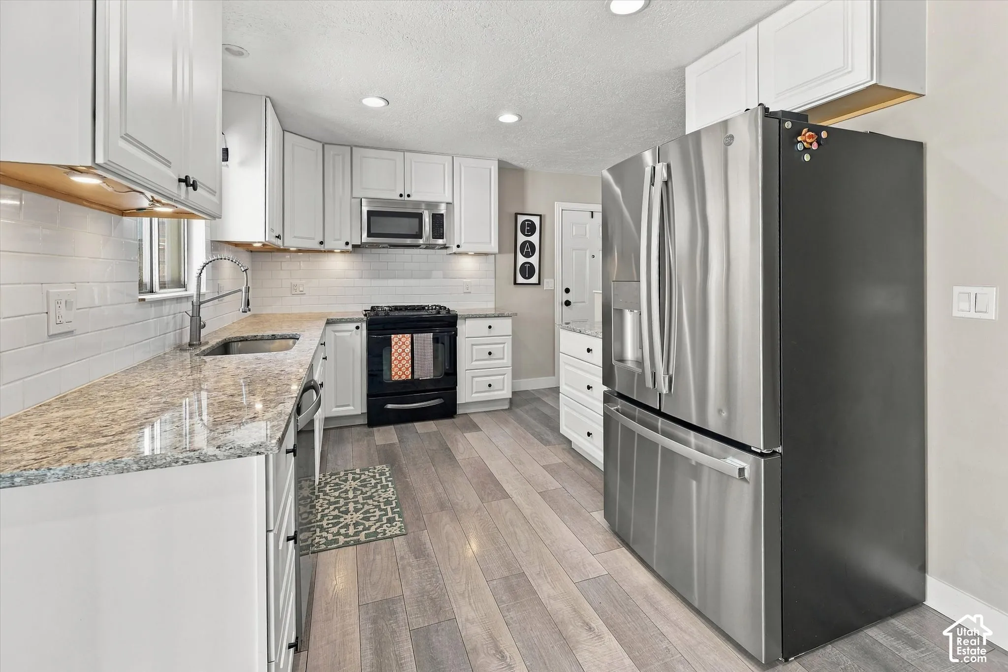 Kitchen featuring white cabinetry, stone-surface countertops, subway tile backsplash, wood-finish flooring, and stainless steel appliances