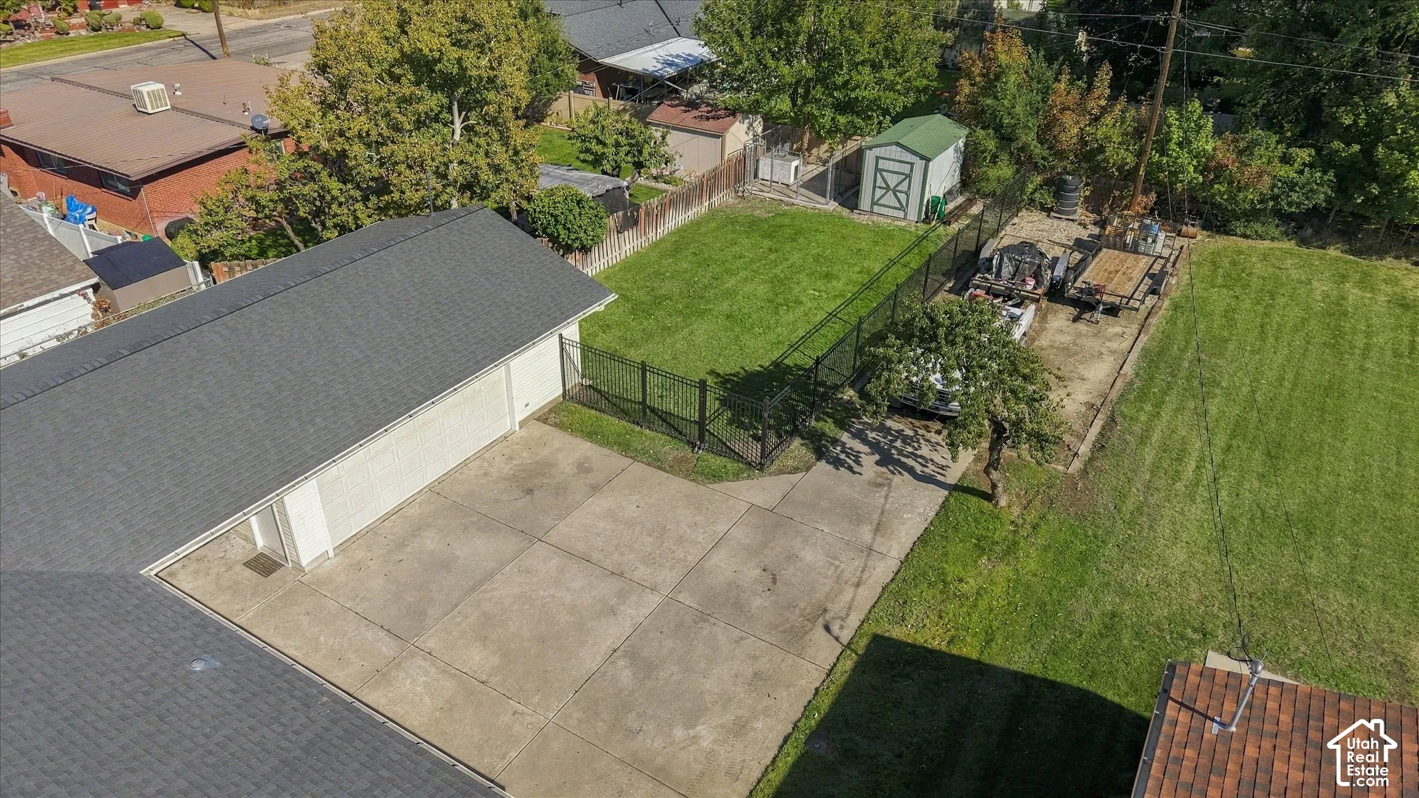 Large lot featuring a concrete driveway, multi-car garage, fenced lawn area, and detached storage structure