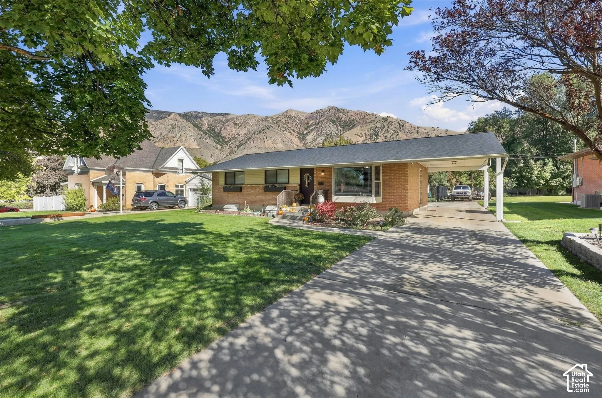 Single-story brick exterior featuring a covered carport, concrete driveway, bay window, and backdrop of mountain scenery