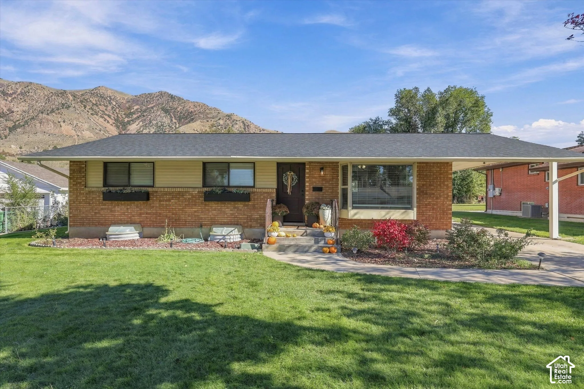 Single-story brick and siding exterior featuring a prominent carport, bay window, and backdrop of mountain scenery