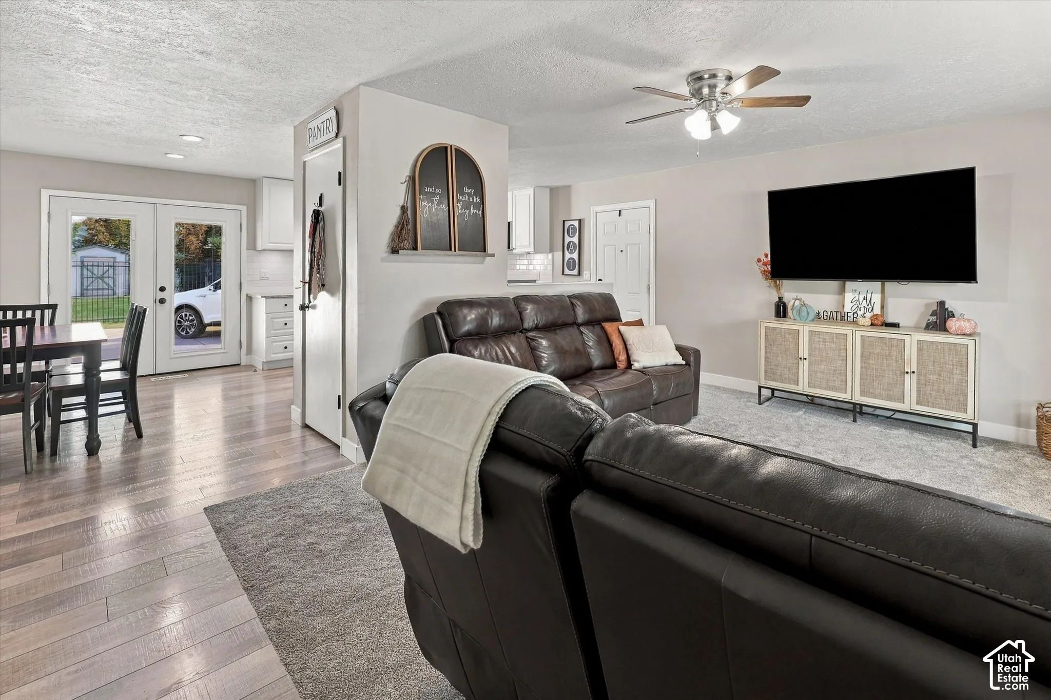 Living area featuring wood-finish flooring, a ceiling fan with integrated lighting, and glass-paneled double doors providing exterior access