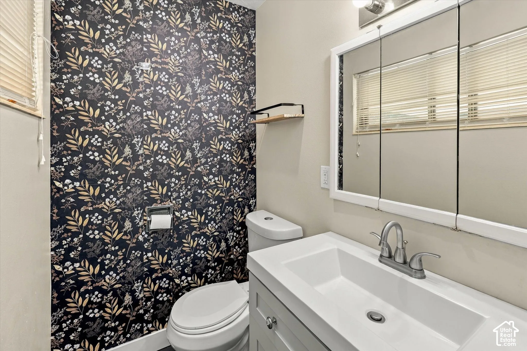 Bathroom featuring a floral-patterned accent wall, white vanity with an integrated sink, brushed-nickel faucet, and a tri-panel medicine cabinet