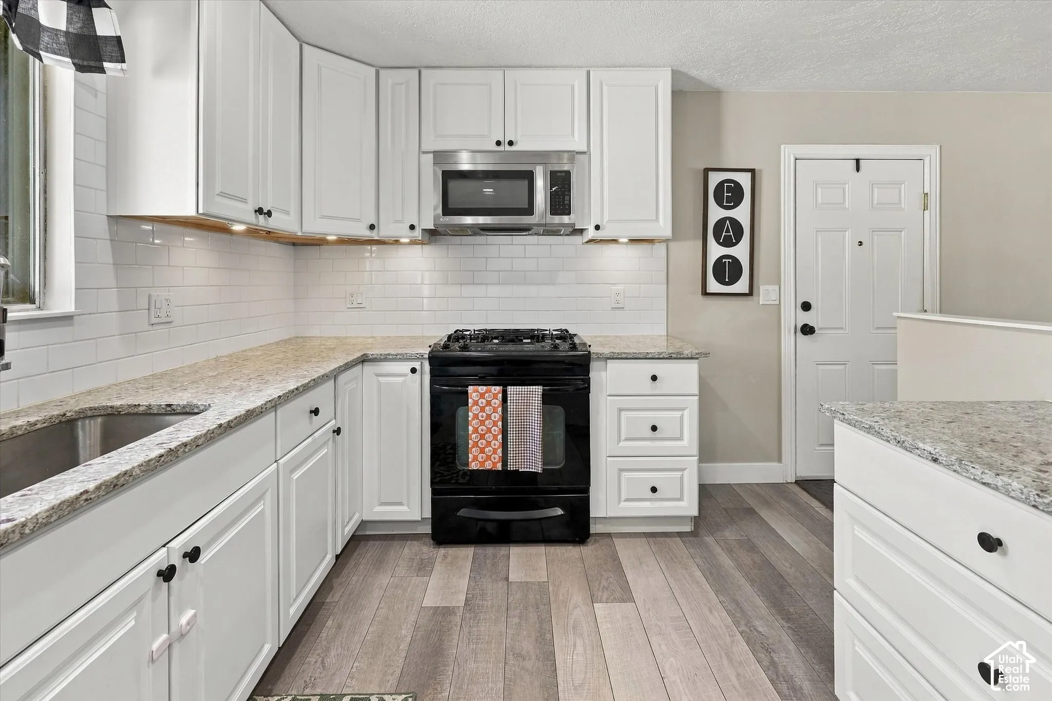 Kitchen featuring white cabinetry, stone-finish countertops, subway tile backsplash, stainless steel microwave, and wood-finish flooring