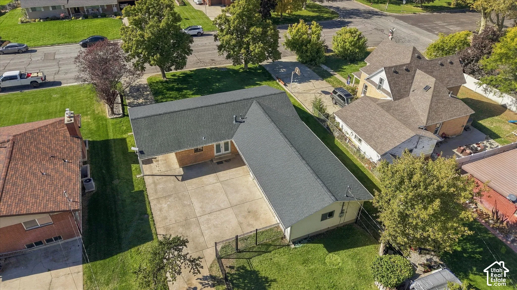 L-shaped residence featuring an asphalt shingle roof, expansive concrete driveway, and chain-link fencing