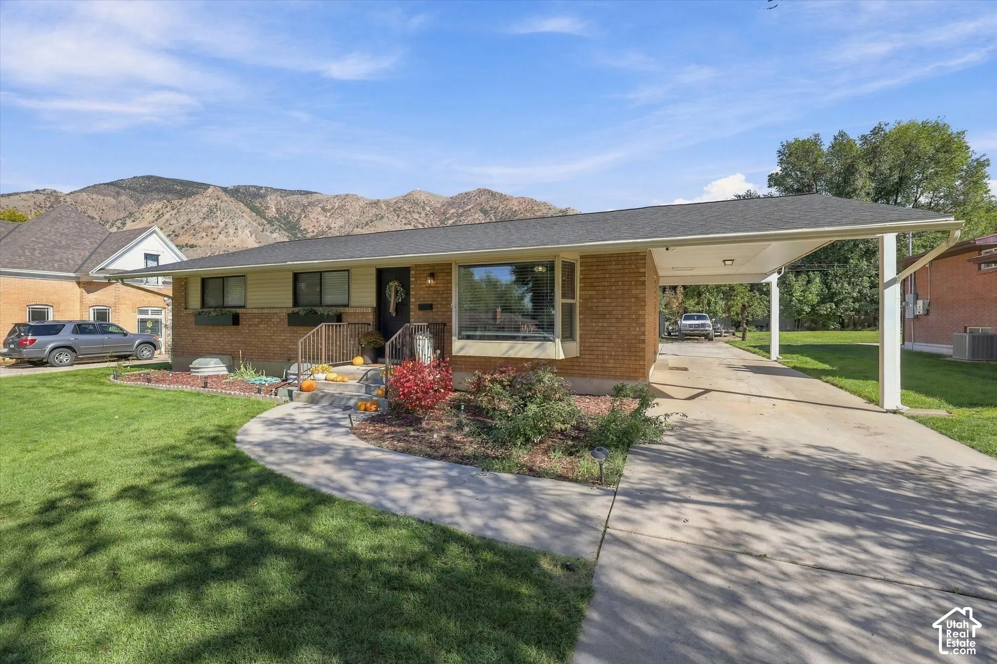 Single-story brick exterior featuring a covered carport, large picture window, and mountain backdrop