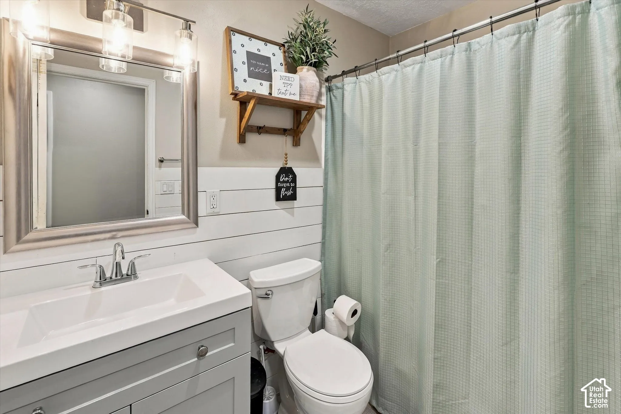 Bathroom featuring white shiplap walls, a vanity with a rectangular sink, brushed nickel hardware, and a framed vanity mirror with an attached three-light fixture