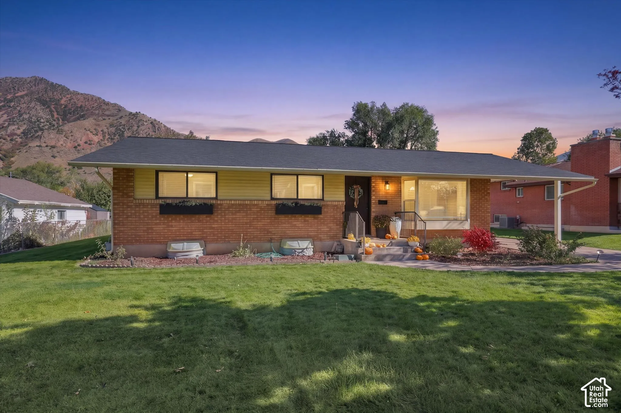 Single-level exterior featuring a brick and siding facade, covered carport, large picture window, mountain backdrop, and expansive front lawn