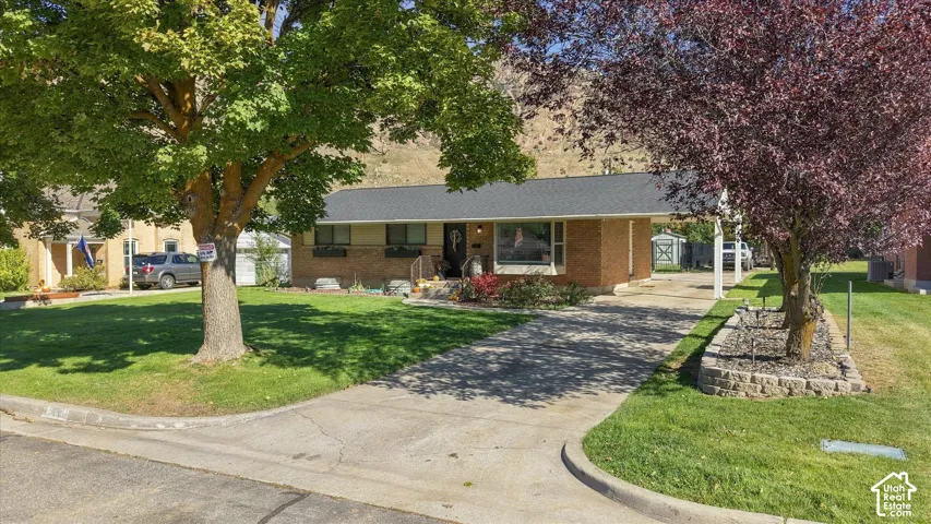 Single-story brick exterior residence featuring a covered carport, concrete driveway, and tiered stone landscaping wall