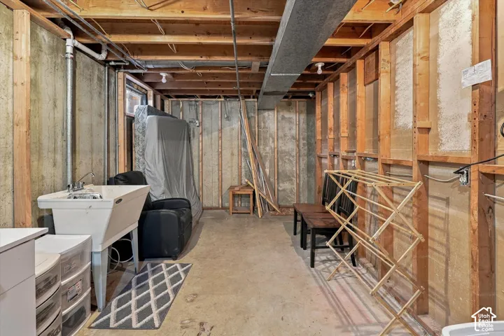 Unfinished utility area featuring exposed wood stud wall framing, concrete foundation walls, a concrete floor, and a utility sink