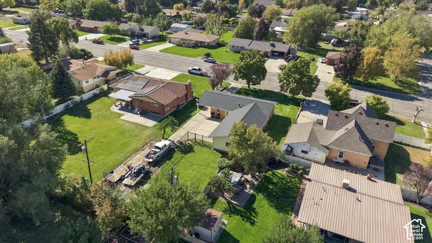 Aerial perspective featuring a residential lot with a manicured lawn, paved concrete driveway, and established mature trees