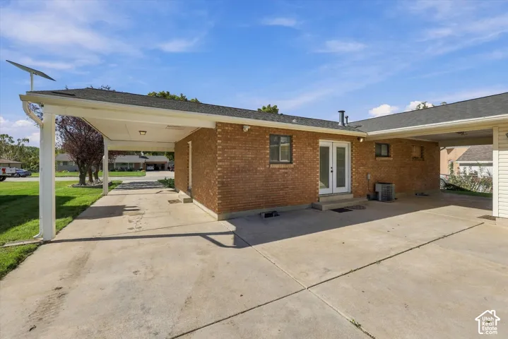 Brick exterior facade featuring a dual carport, expansive concrete driveway, and white-framed French doors