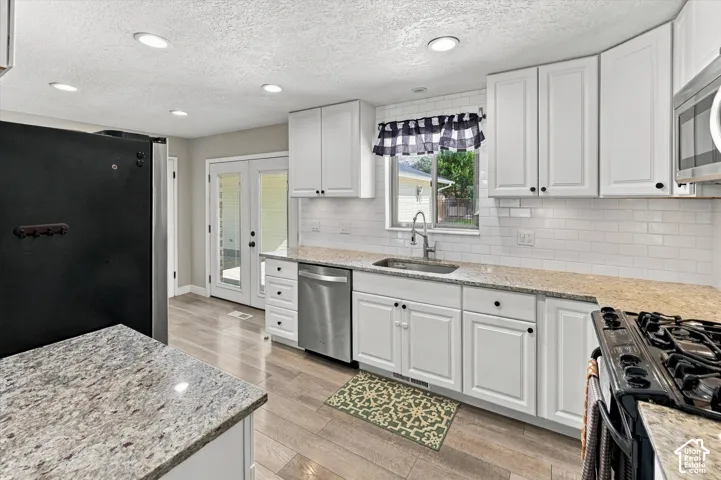Kitchen featuring white shaker-style cabinetry, stone-finish countertops, subway tile backsplash, stainless steel appliances, and wood-finish flooring