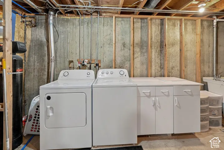 Laundry area featuring built-in white cabinetry, concrete foundation walls, exposed wood framing, and integrated water filtration system