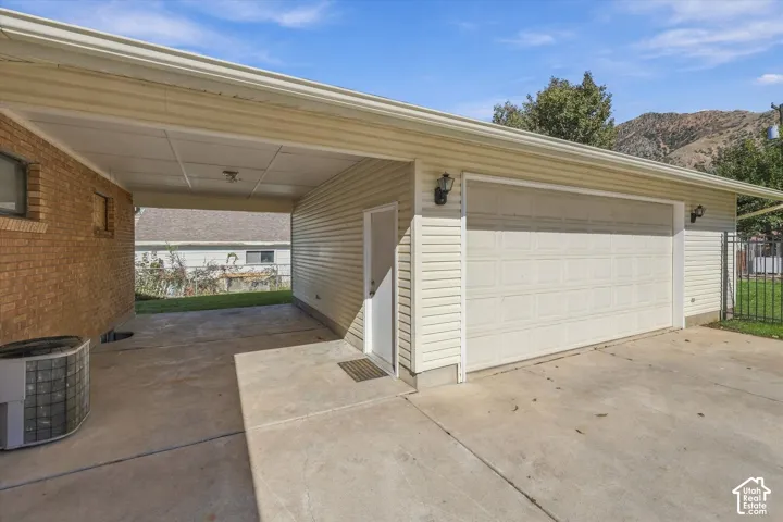 Attached two-car garage with horizontal siding, covered carport area, concrete driveway, and exterior wall-mounted lighting