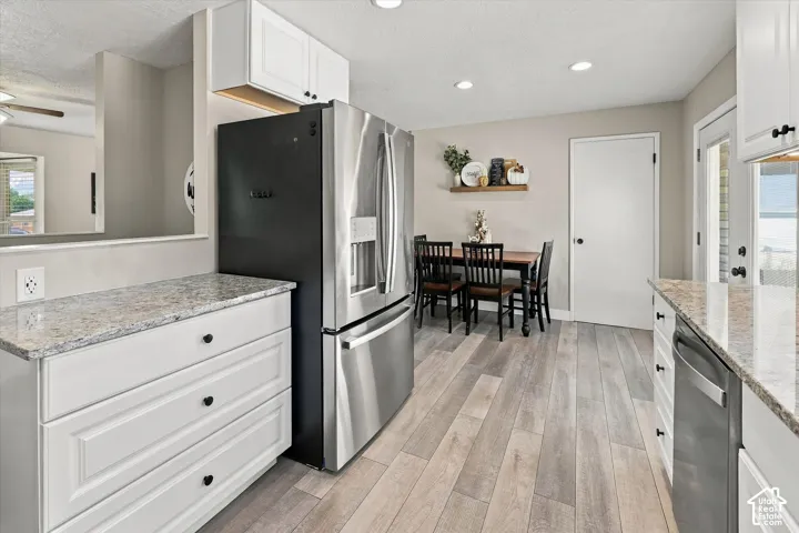 Kitchen featuring white shaker-style cabinetry, stone-finish countertops, stainless steel appliances, wood-finish flooring, and recessed ceiling lighting