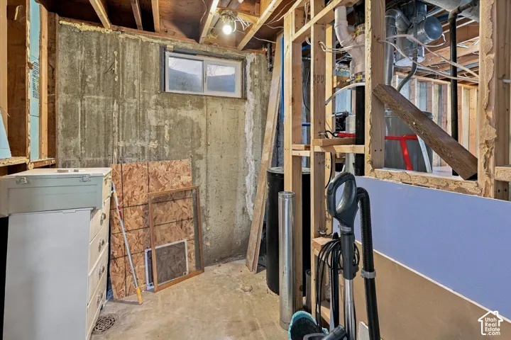 Unfinished basement area featuring exposed wood framing, concrete foundation walls, a sliding window, and exposed plumbing infrastructure