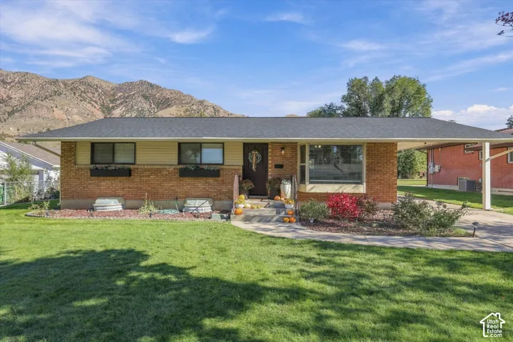 Single-story brick and siding exterior featuring a prominent carport, bay window, and backdrop of mountain scenery