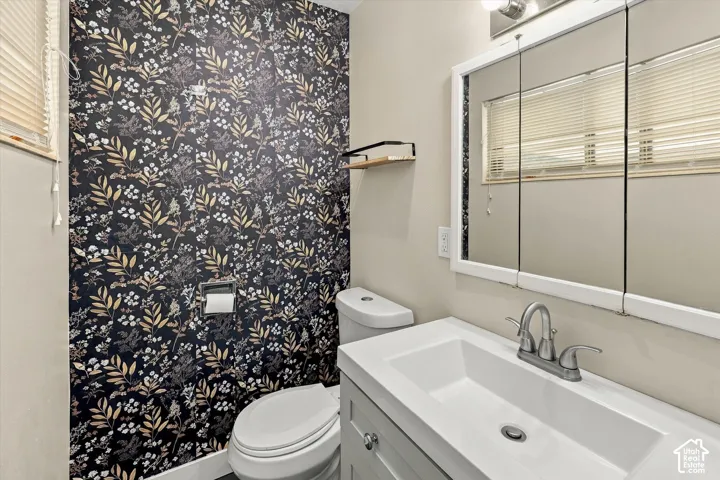 Bathroom featuring a floral-patterned accent wall, white vanity with an integrated sink, brushed-nickel faucet, and a tri-panel medicine cabinet