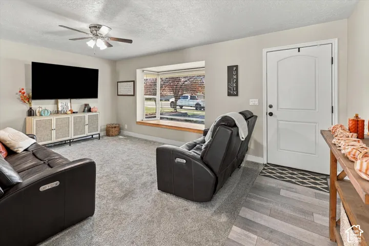 Living area featuring a large bay window with a built-in bench, neutral carpeting, a ceiling fan with integrated lighting, and a solid-core exterior door