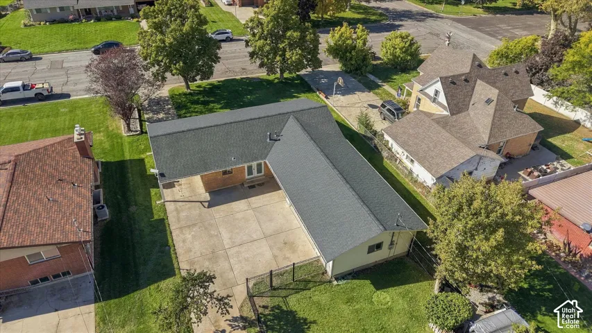 L-shaped residence featuring an asphalt shingle roof, expansive concrete driveway, and chain-link fencing