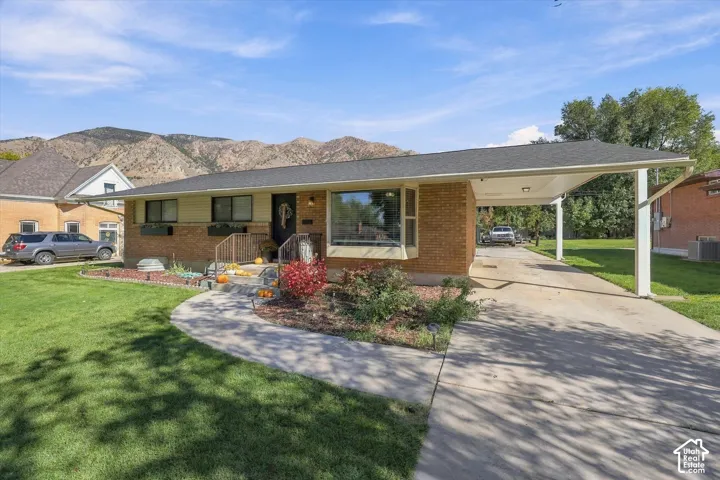 Single-story brick exterior featuring a covered carport, large picture window, and mountain backdrop