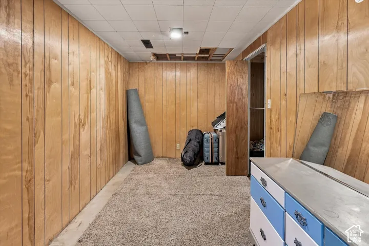 Room featuring wood-paneled walls, a drop ceiling, and carpeted flooring
