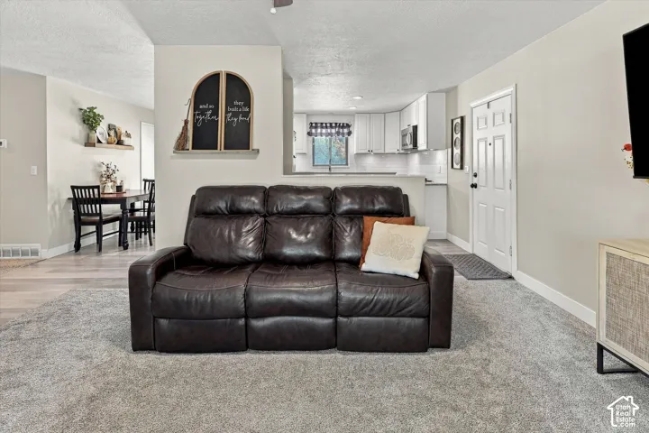 Open-concept interior featuring neutral wall tones, carpeted flooring, wood-finish flooring, white kitchen cabinetry, and a six-panel entry door
