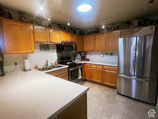 Kitchen featuring solid wood cabinetry, stainless steel appliances, solid-surface countertops, dual-basin stainless steel sink, and track lighting