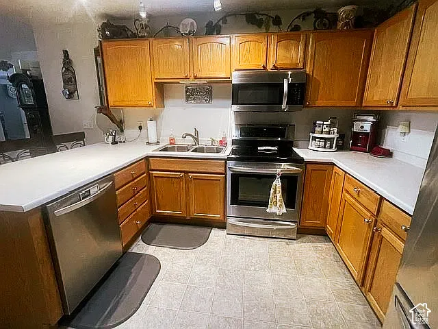 Kitchen featuring wood cabinetry, stainless steel appliances, dual-basin sink with a gooseneck faucet, and laminate countertops