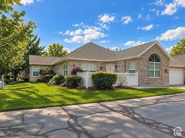 Single-story brick exterior featuring a hip roof, arched window with decorative muntins, white vinyl fencing, and mature landscaping