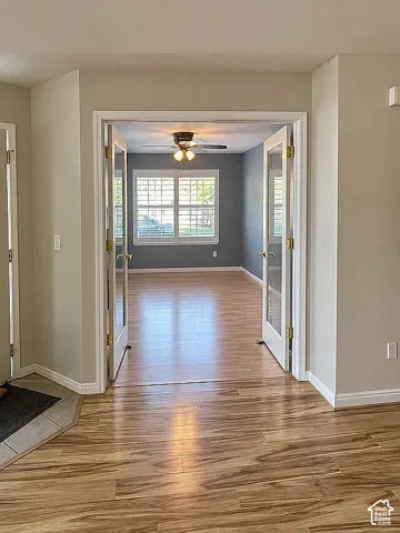 Double French doors with glass panes, wood-finish flooring, multi-pane window with shutters, and a ceiling fan with integrated lighting