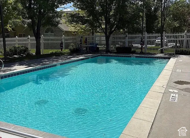 In-ground swimming pool featuring a concrete surround, metal perimeter fencing, and mature tree landscaping