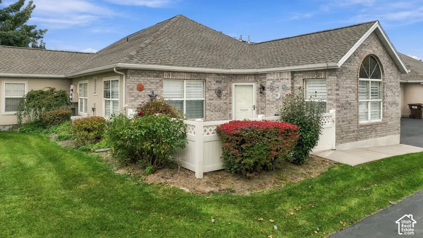 Single-story exterior featuring multi-toned brick masonry, a high-pitch hip roof, arched window detailing, and a white lattice-style privacy fence