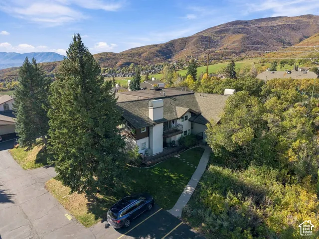Multi-level exterior featuring a shingled roof, stucco siding, a stone chimney, and a backdrop of mountain scenery