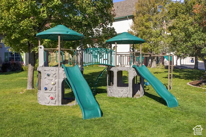 Backyard featuring a permanent multi-level play structure with dual slides, climbing elements, and canopy covers set within a landscaped lawn