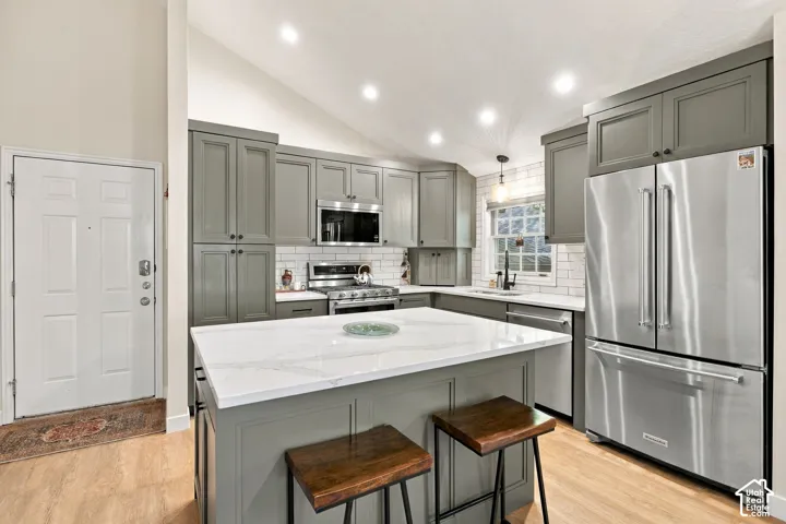 Kitchen featuring shaker-style cabinetry, a central island with a stone countertop, stainless steel appliances, a white subway tile backsplash, and vaulted ceilings