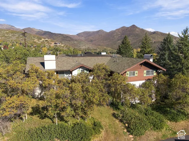 Multi-level exterior featuring a shingle roof, white chimneys, decorative shutters, and wooded surroundings set against a mountain backdrop