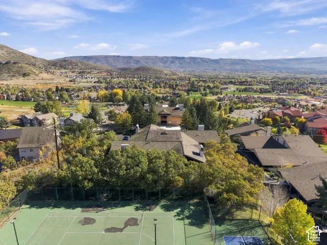 Fenced tennis court with mountain range backdrop, mature trees, and expansive area landscape
