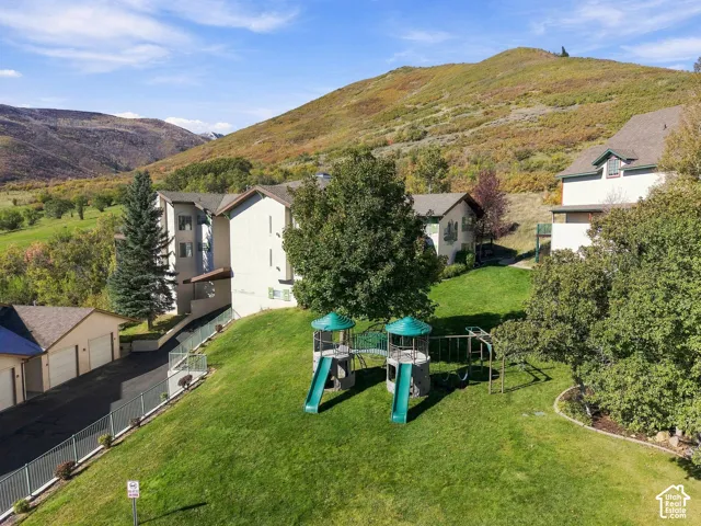 Ground-level exterior featuring a multi-story building, attached garage structures, expansive green space, mature trees, and mountain scenery