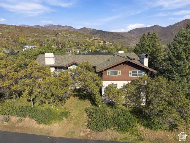 Two-story residence featuring wood and stucco exterior cladding, dual masonry chimneys, decorative shutters, and expansive mountain terrain