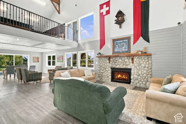 Vaulted ceiling, full-height river rock fireplace with wood mantel, wood-finish flooring, and mezzanine level featuring decorative metal railings