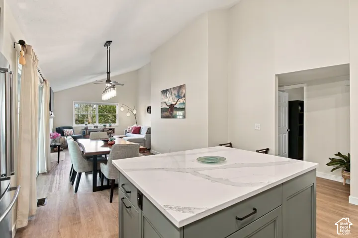 Kitchen island featuring a solid-surface countertop and shaker-style cabinetry with matte black hardware, accented by wood-finish flooring and vaulted ceilings
