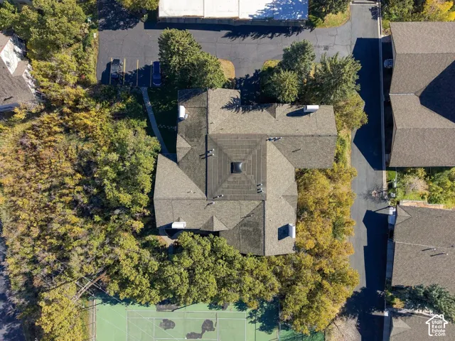 Aerial perspective featuring a multi-faceted shingle roof, integrated skylight, paved surface parking, and a dedicated tennis court surrounded by mature trees