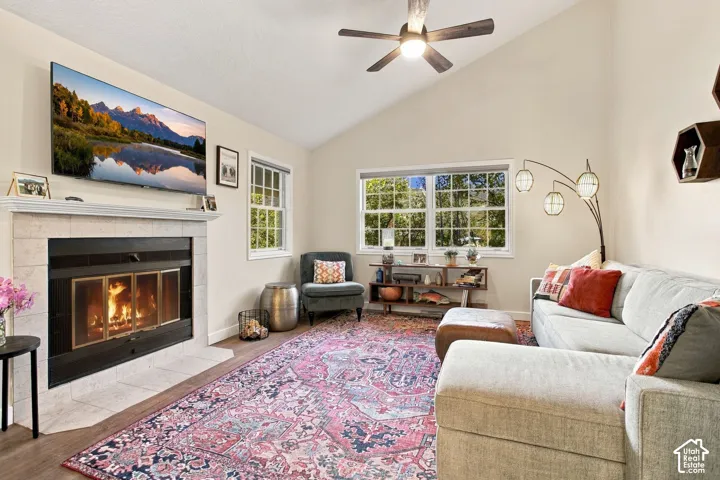 Vaulted ceiling featuring a ceiling fan, stone-surround fireplace with a mantel, and multi-pane windows
