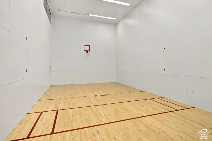 Multi-purpose sports court featuring wood-finish flooring, smooth wall paneling, high ceilings with recessed lighting, and a built-in wall-mounted hoop