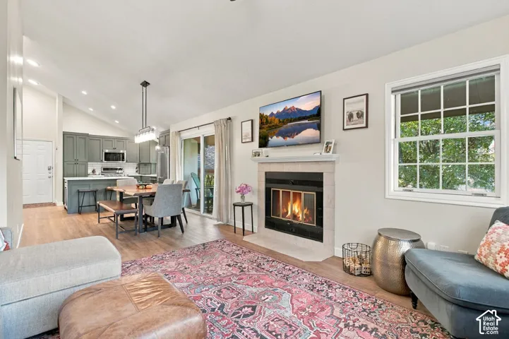 Open-concept interior featuring vaulted ceilings, a central fireplace with a tiled surround, wood-finish flooring, recessed lighting, and sliding glass doors