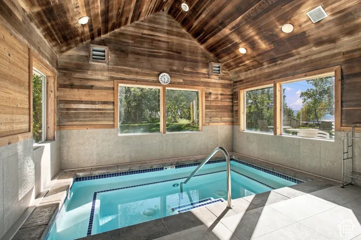 Indoor pool featuring wood-paneled vaulted ceilings, tile surround, inset lighting, and large windows