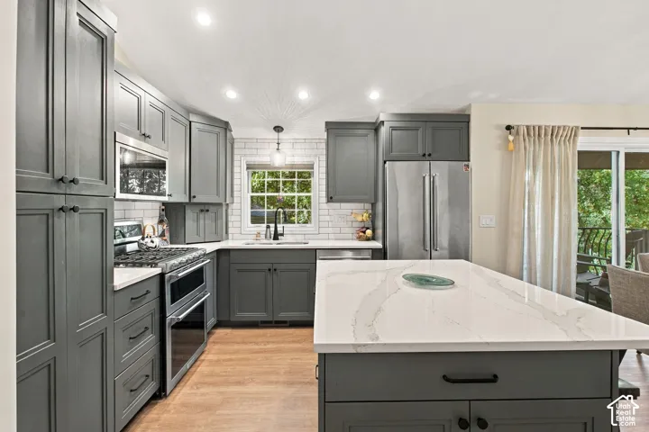 Kitchen featuring dark grey shaker-style cabinetry, a central island with a white quartz countertop, subway tile backsplash, stainless steel appliances, and wood-finish flooring